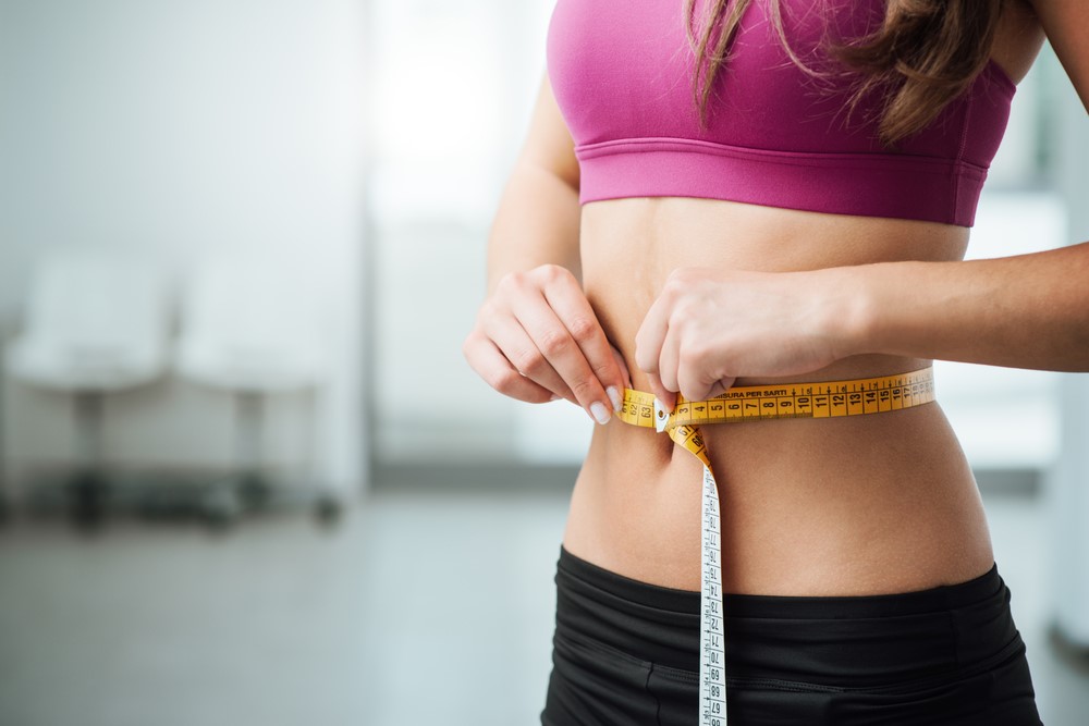 Slim young woman measuring her thin waist with a tape measure, close up